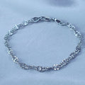 A close-up view of a White Gold Plated  anchor mariner link bracelet with textured links on a soft, reflective, light-blue fabric surface – Aurora Jewelry.