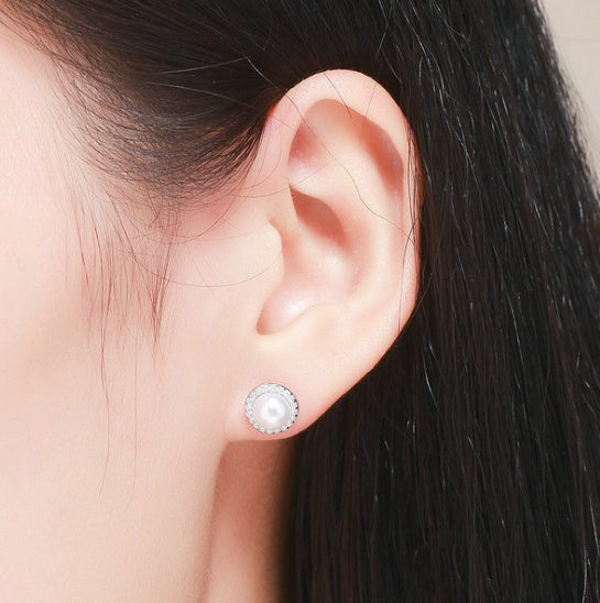 Close-up of an ear wearing a pearl stud earring with dark hair in the background