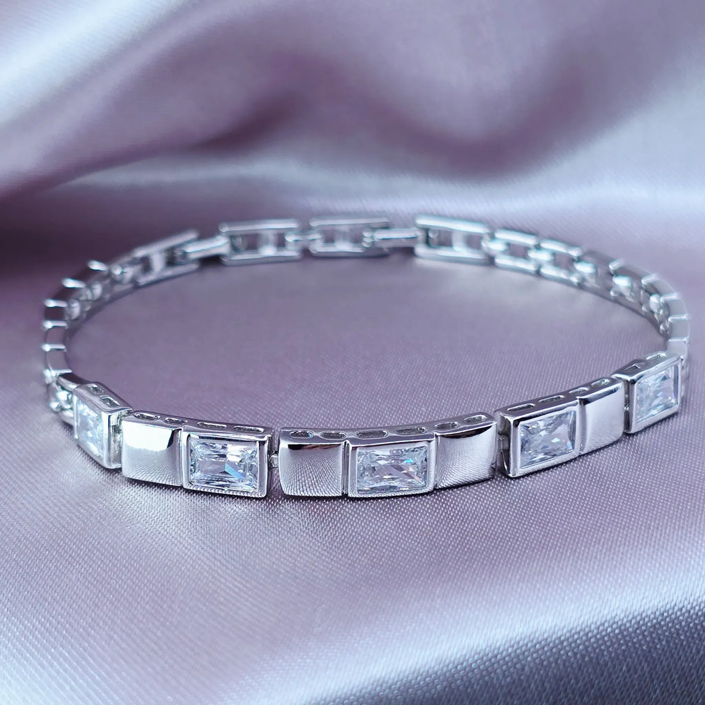 Silver bracelet with square-cut gemstones on a soft pink fabric background