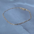 High-shine gold-plated Figaro link bracelet displayed on a white satin fabric background – Aurora Jewelry Collection