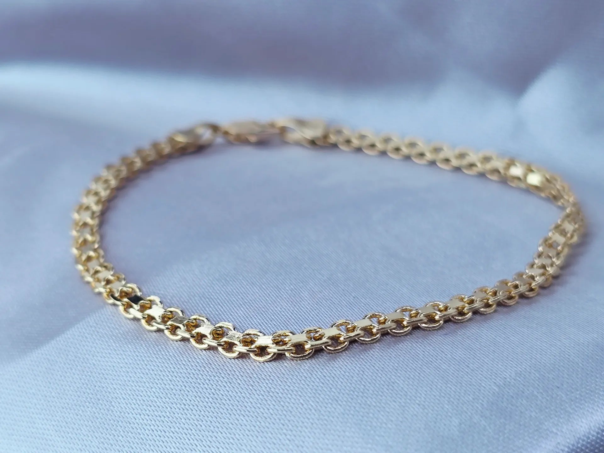 Close-up of a gold-plated textured round link bracelet on a soft blue satin background