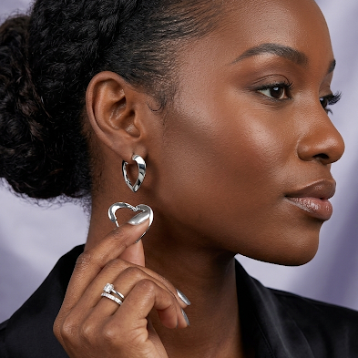 Woman wearing silver heart-shaped earrings and rings against a blurred background
