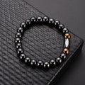 Black beaded bracelet with brown and white accents on a textured black surface