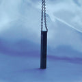 Black cylindrical pendant on a chain against a blue fabric background