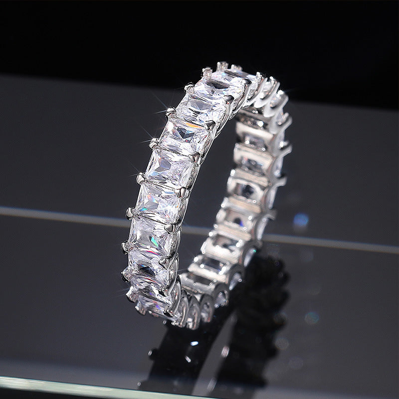 Silver ring with clear gemstones on a reflective black surface