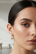 Close-up of a woman wearing gold hoop earrings with a neutral background