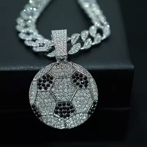 Silver pendant shaped like a soccer ball with black accents on a chain against a dark background